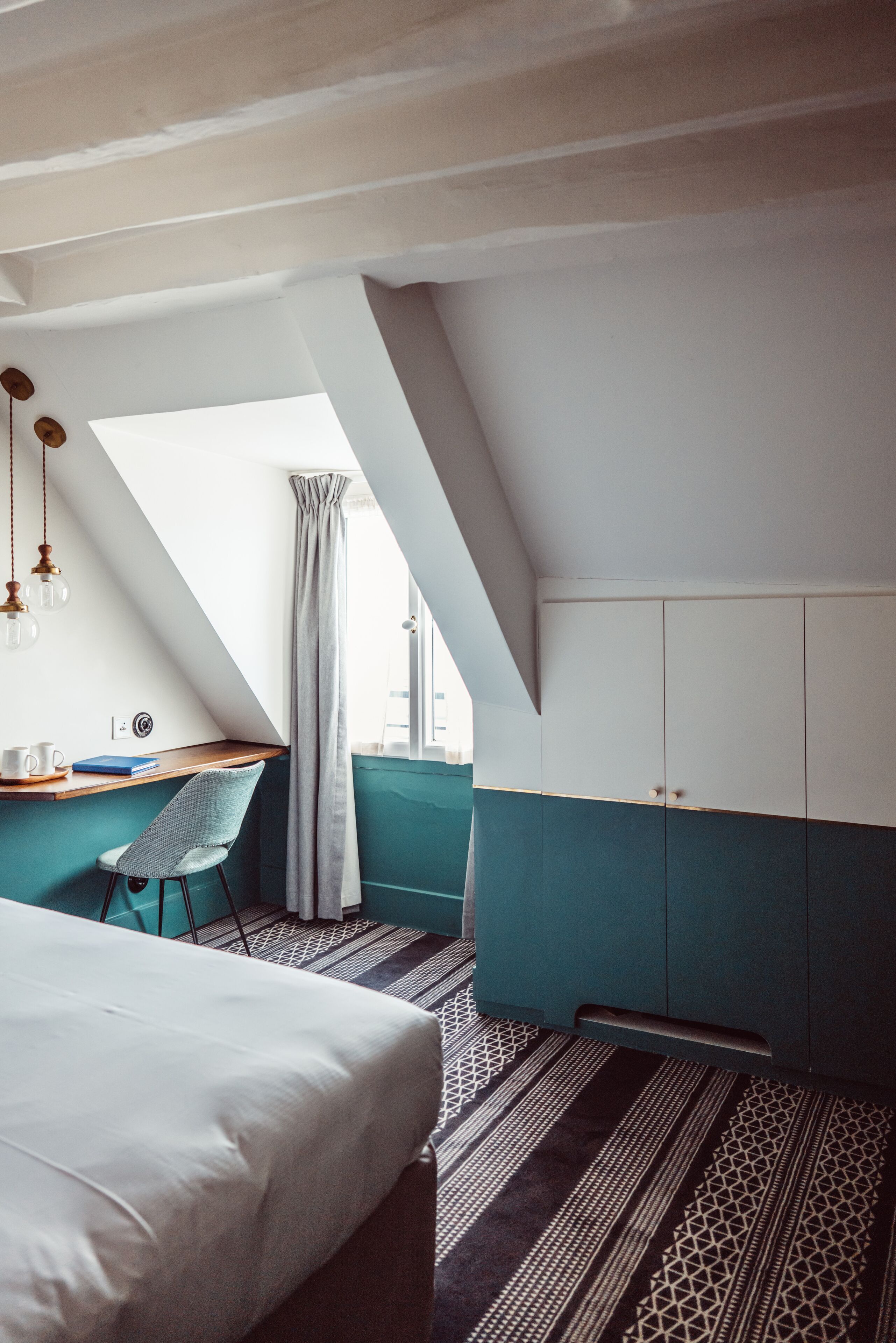 Una habitación de hotel moderna con techo inclinado, una cama, un escritorio con silla y un armario.