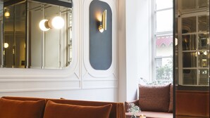 A modern interior with a velvet orange sofa, a round table with candles, and a large mirror. - Hotel Panache (Paris)