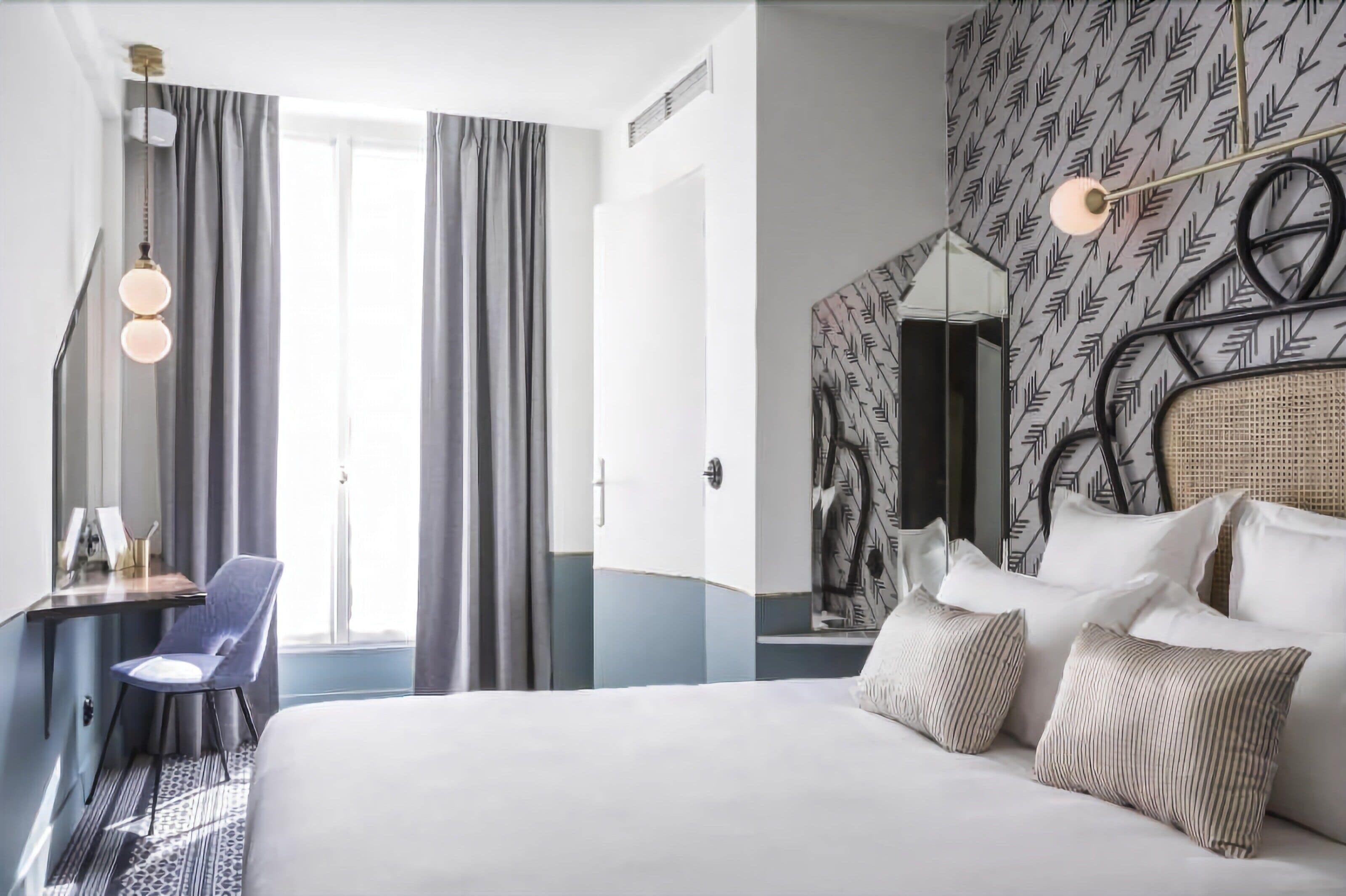 Une chambre d’hôtel avec un lit, un bureau et une chaise, ainsi qu’une grande fenêtre avec des rideaux.