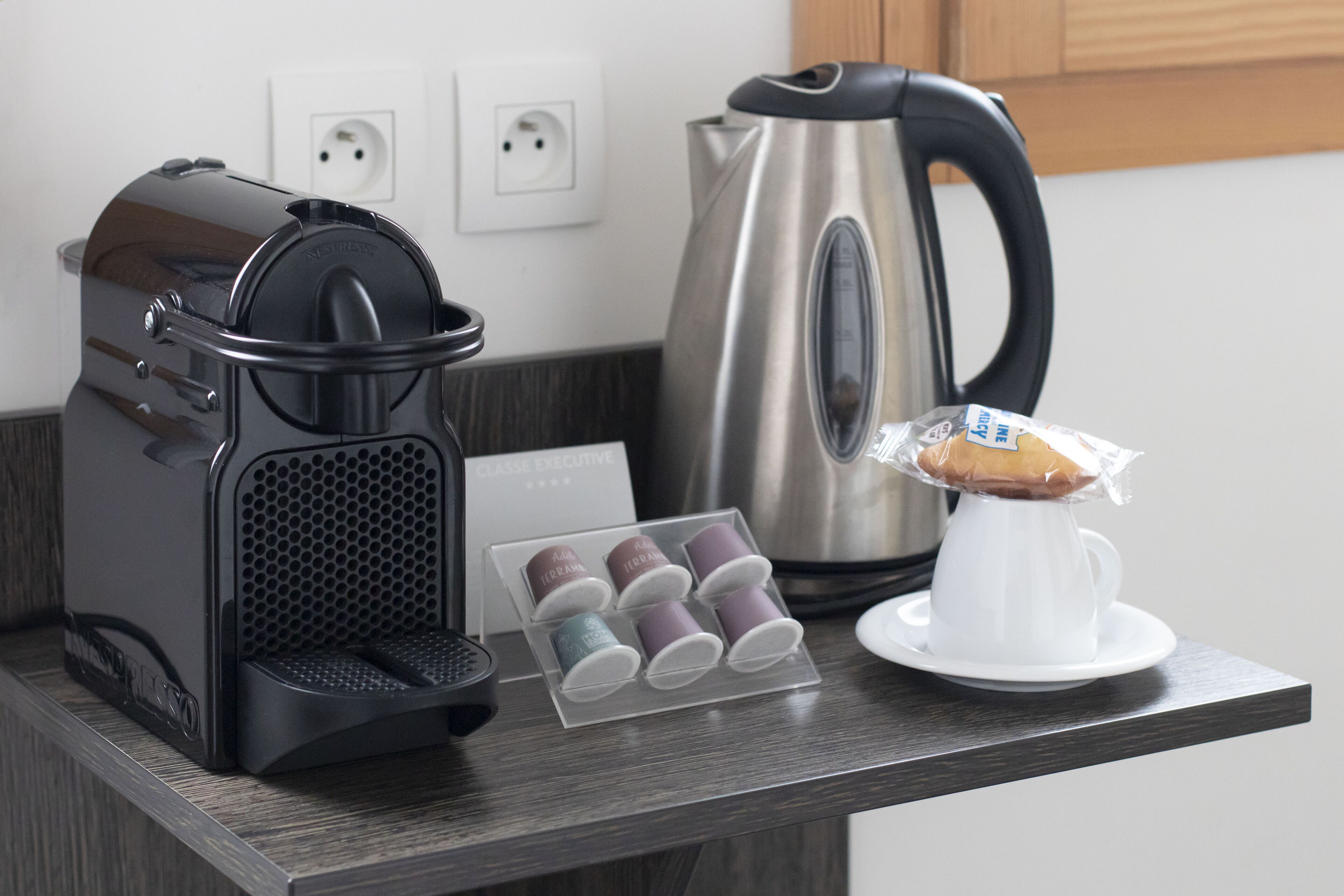 A kitchen counter with a coffee maker, a kettle, and a muffin display.
