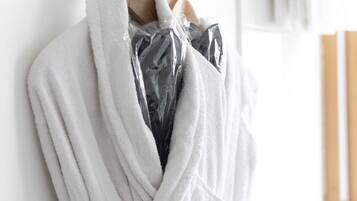 Ein weißer Bademantel hängt an einem Metallhaken in einem Badezimmer mit einem hölzernen Handtuchhalter und einem weißen Handtuch im Hintergrund.