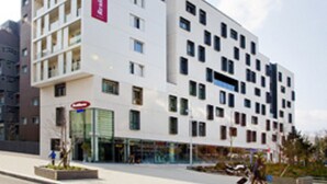 Un hôtel moderne à la façade blanche, avec de nombreux étages et une grande enseigne rouge bien visible sur le côté.