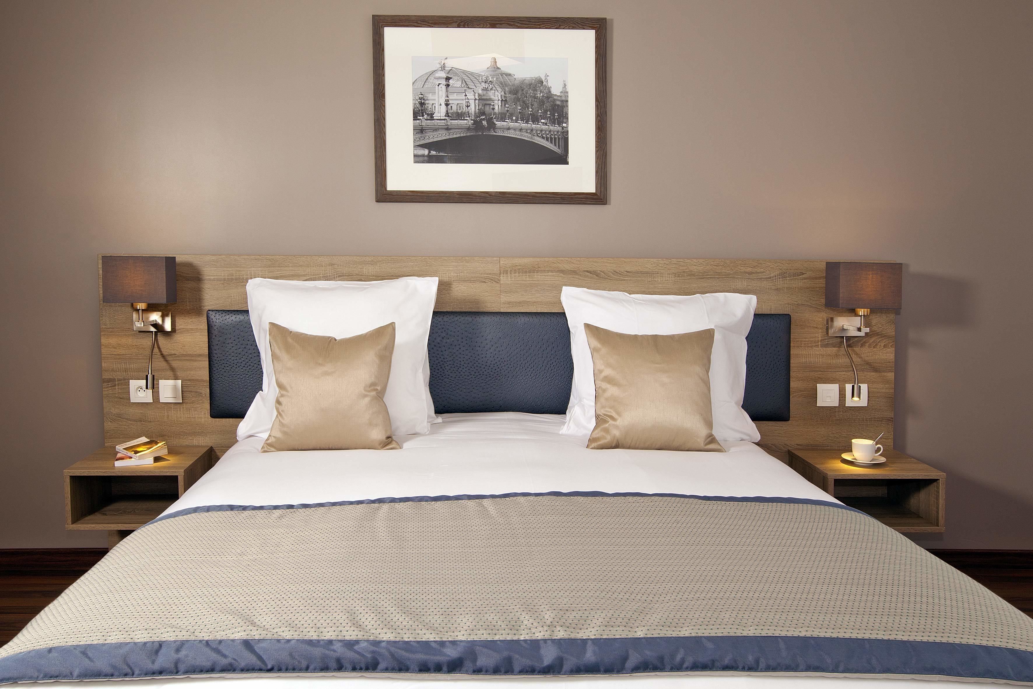 A hotel room with a large bed, two bedside tables, a framed picture on the wall, and a nightstand with a cup.