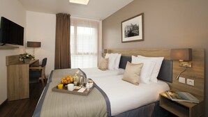 Une chambre d’hôtel avec un lit, un bureau, une télévision et une fenêtre avec des rideaux.
