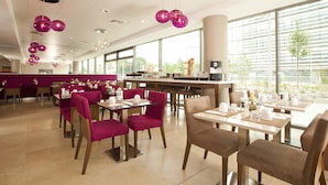 Un espace repas moderne, doté de tables et de chaises, de grandes fenêtres et d’un éclairage décoratif.