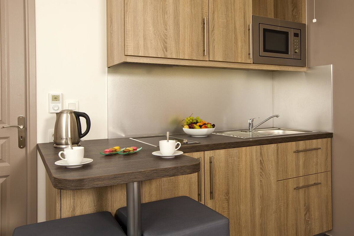 Een compacte kitchenette met een magnetron, een koffiezetapparaat en een schaal met fruit op het aanrecht.