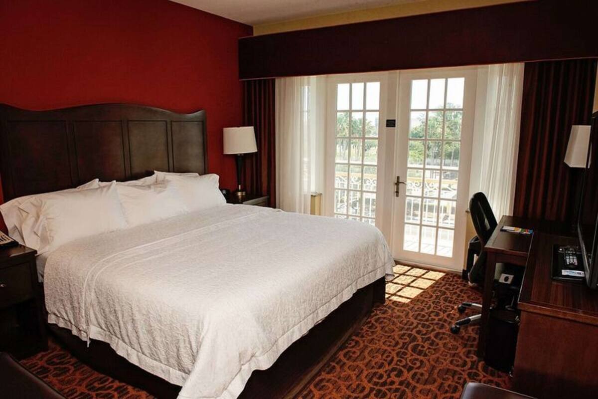 A hotel room with a large bed, a desk with a computer, a chair, and a window with curtains.