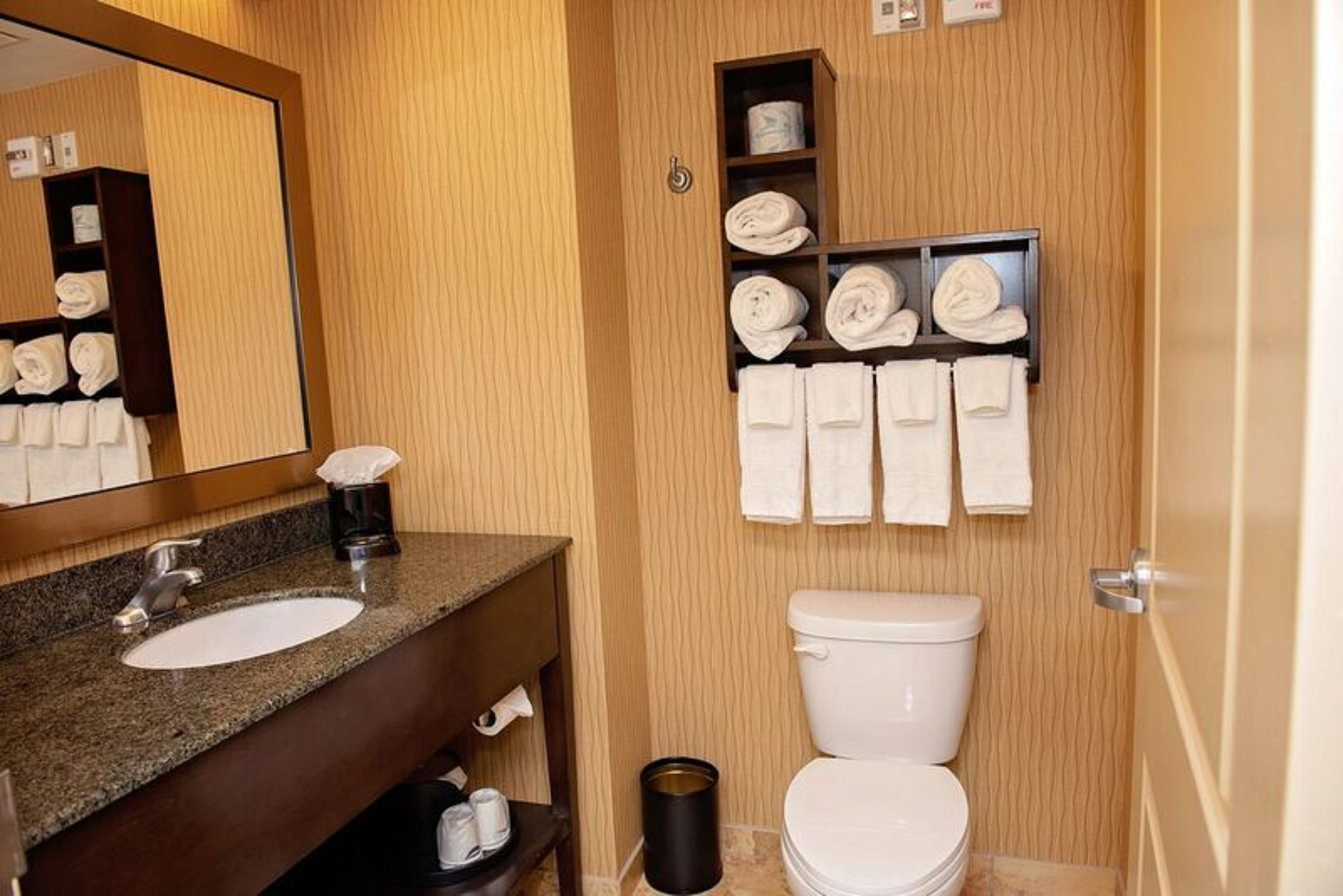 A hotel bathroom with a granite sink, white toilet, and towel racks.