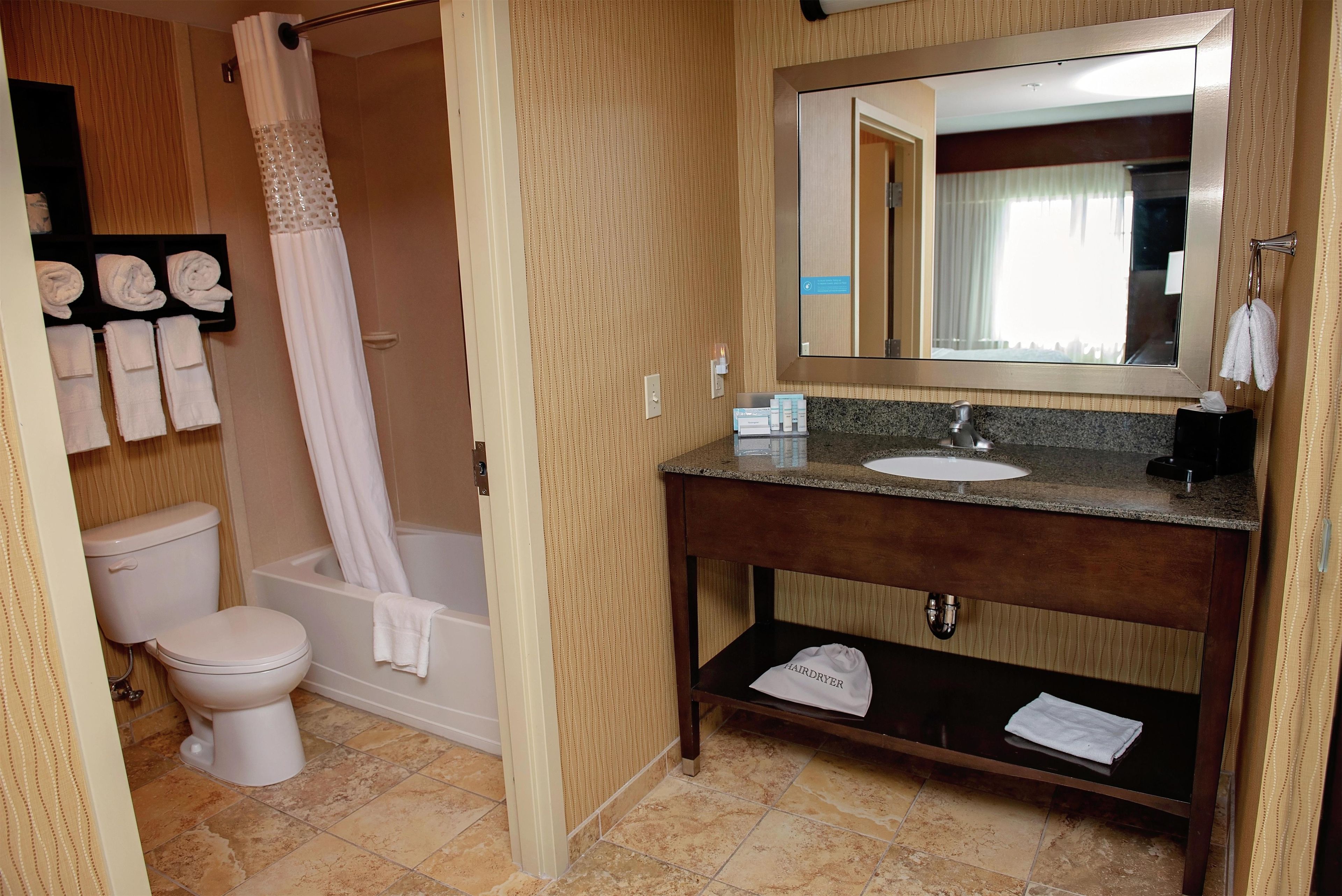A bathroom with a toilet, shower, sink, and mirror.