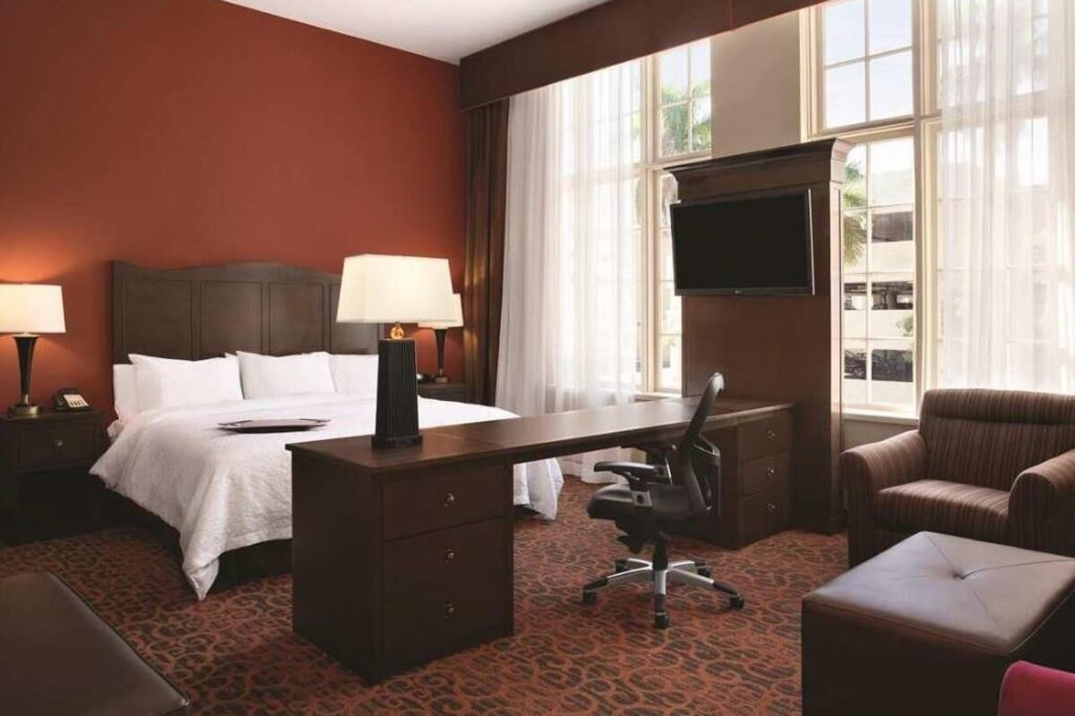 A hotel room with a bed, desk, office chair, and a TV.