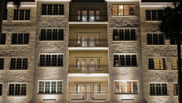 A multi-story hotel with balconies, a ground-level shop, and parked cars.