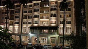 A multi-story hotel with a stone facade, multiple balconies, and a parking lot with several cars.