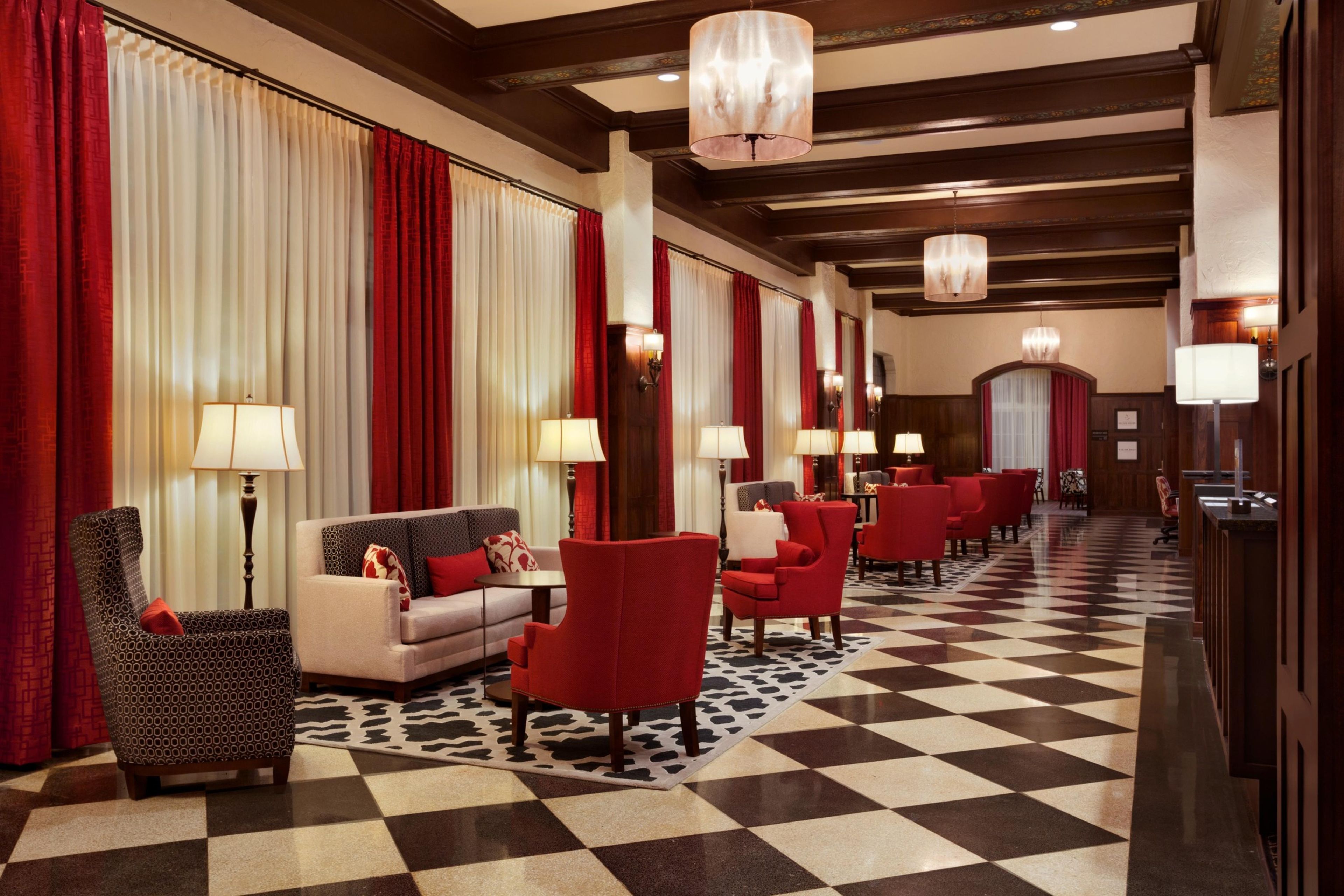 A hotel lobby with a checkered floor, red and white curtains, and multiple seating areas with lamps.