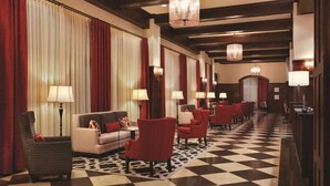 A hotel lobby with a checkered floor, red and white curtains, and multiple seating areas with lamps.