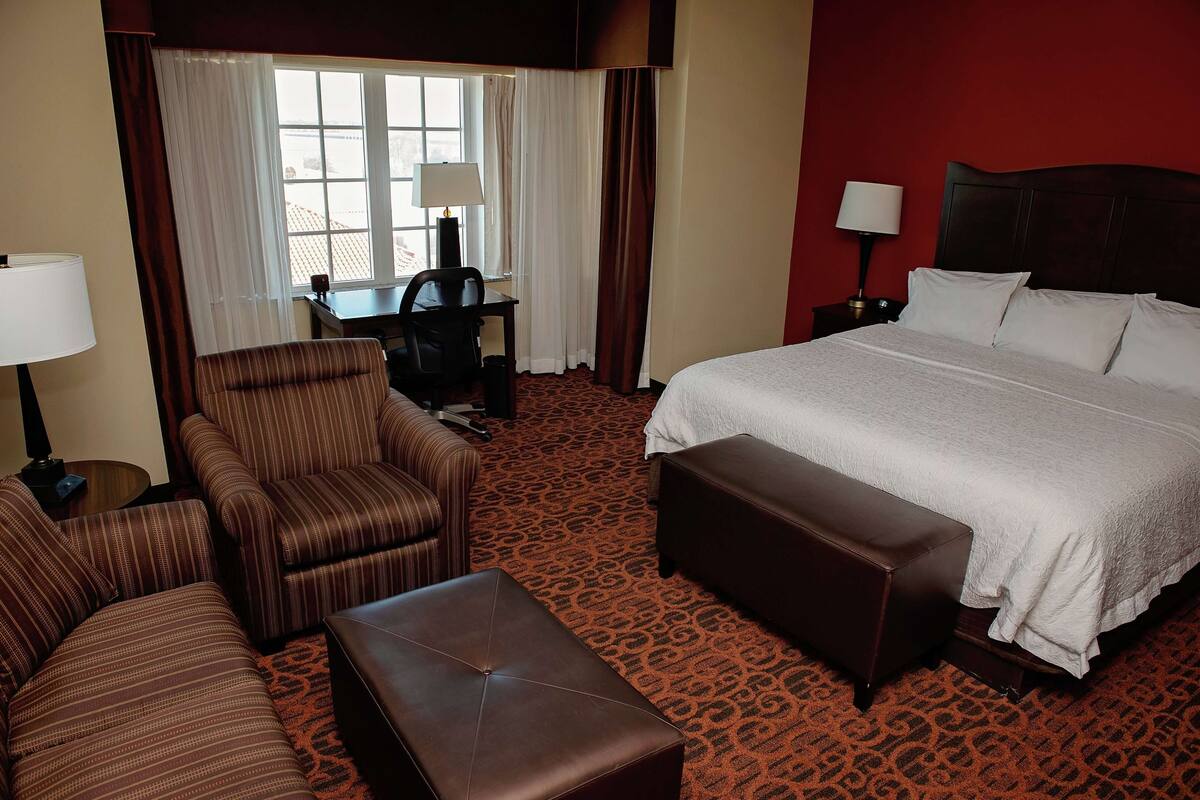 A hotel room with a large bed, a desk, a chair, and a small table.