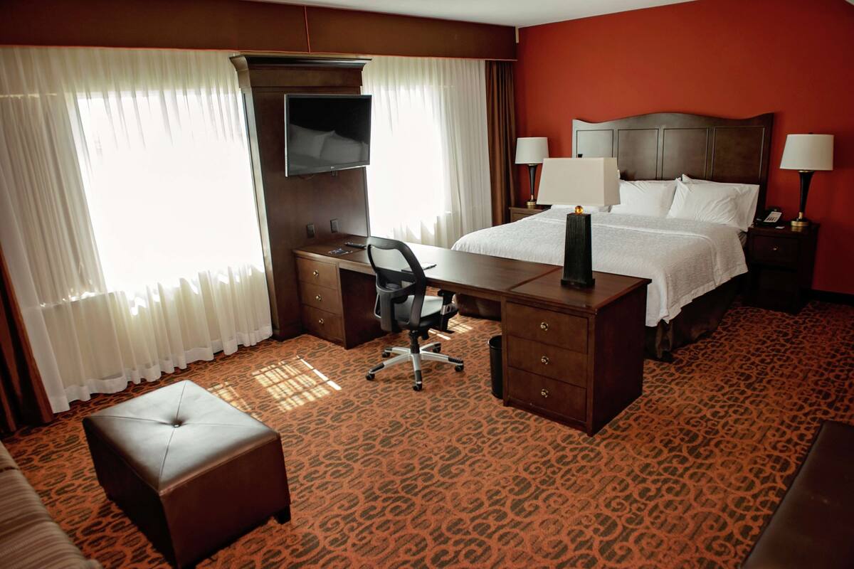 A hotel room with a bed, desk, chair, and a television.