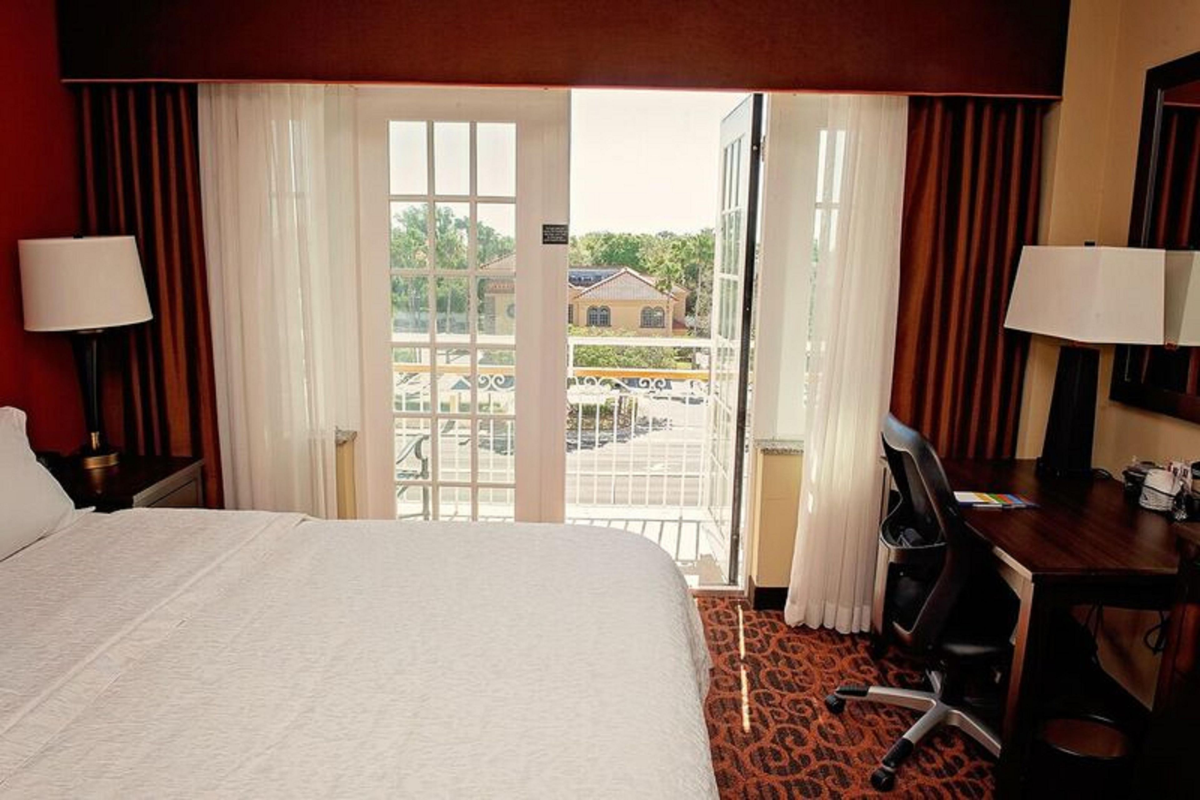 A hotel room with a large bed, a desk, and a view of a building through the window.