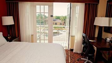A hotel room with a large bed, a desk, and a view of a building through the window.