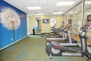 Un gimnasio con cintas de correr, una decoración de diente de león y una pantalla de televisión.