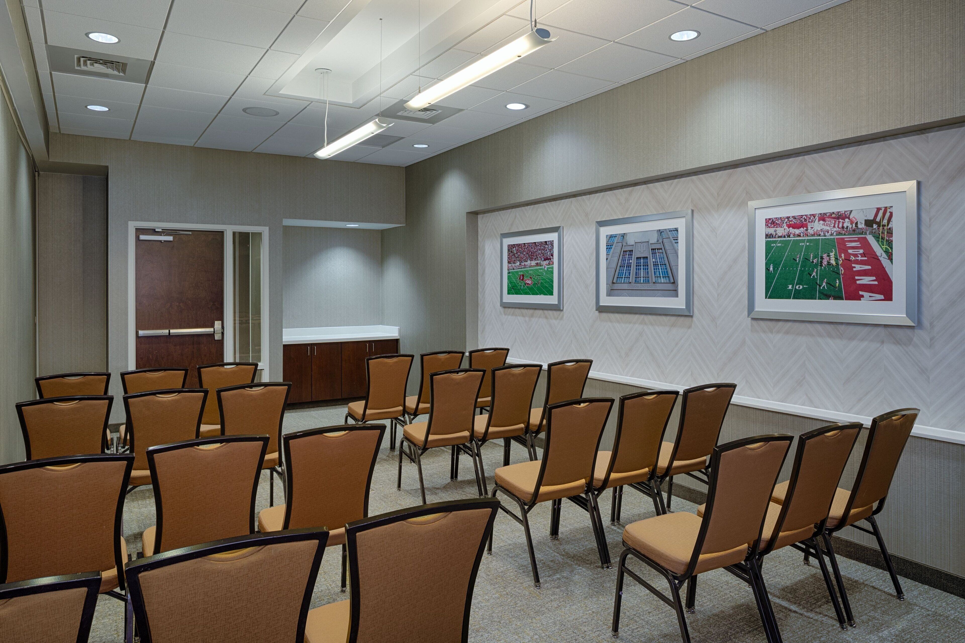 A conference room with rows of chairs, a whiteboard, and framed pictures on the wall.