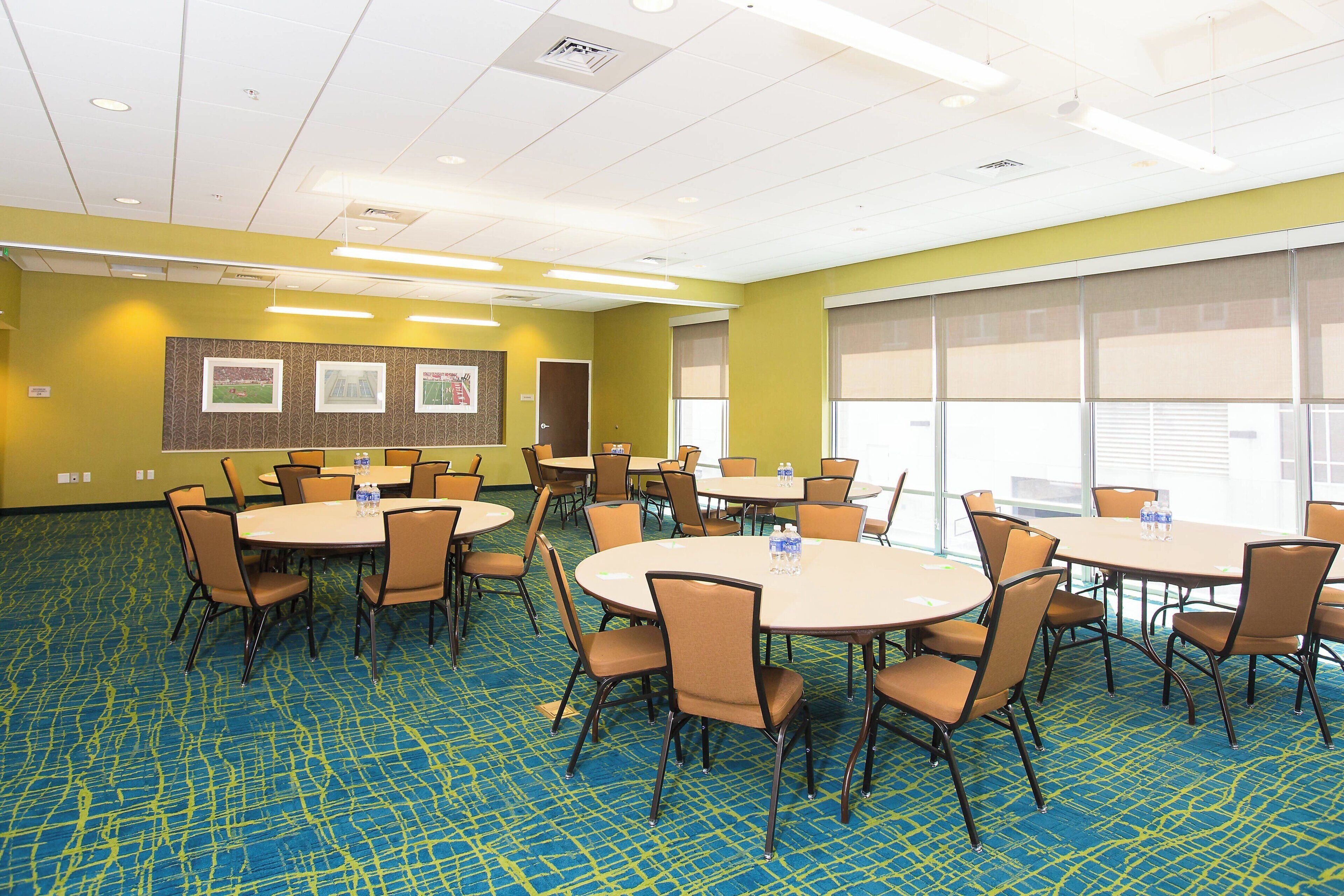 A conference room with multiple tables and chairs, carpeted floor, and large windows.