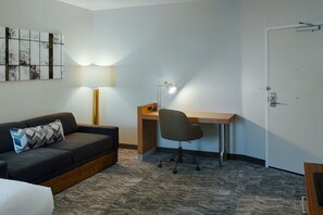 Una habitación de hotel con sofá, escritorio, silla, lámpara y una puerta.
