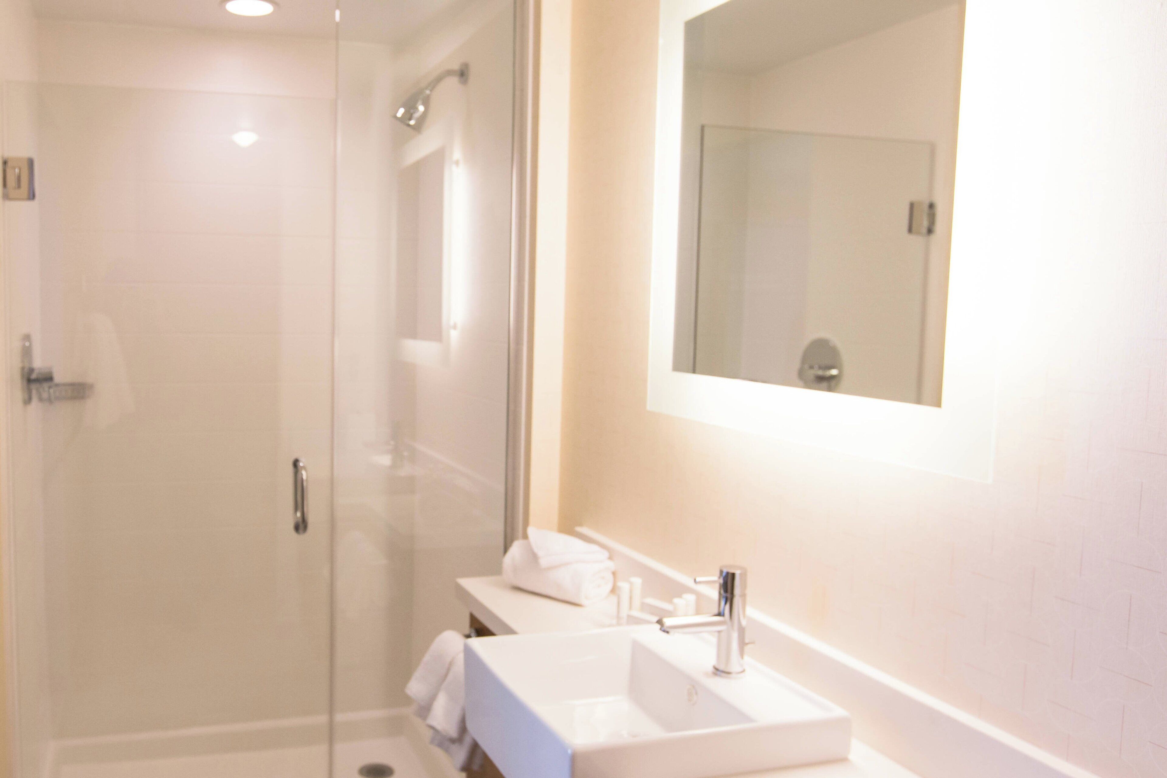Un baño moderno con ducha envuelta en vidrio, un lavamanos blanco y un espejo sobre el mueble.