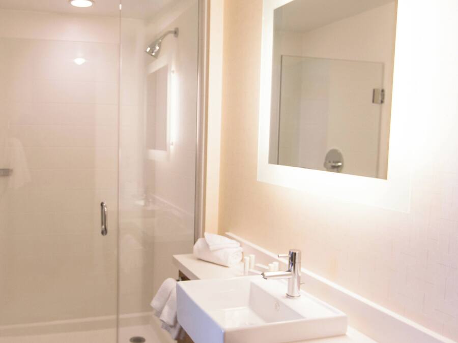 Un baño moderno con ducha envuelta en vidrio, un lavamanos blanco y un espejo sobre el mueble.