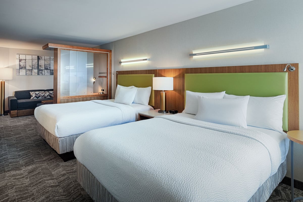 A hotel room with two beds, a sofa, a mirror, and a lamp.