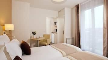 Une chambre d’hôtel avec un lit, une petite table et une chaise, un four à micro-ondes et une fenêtre avec des rideaux.