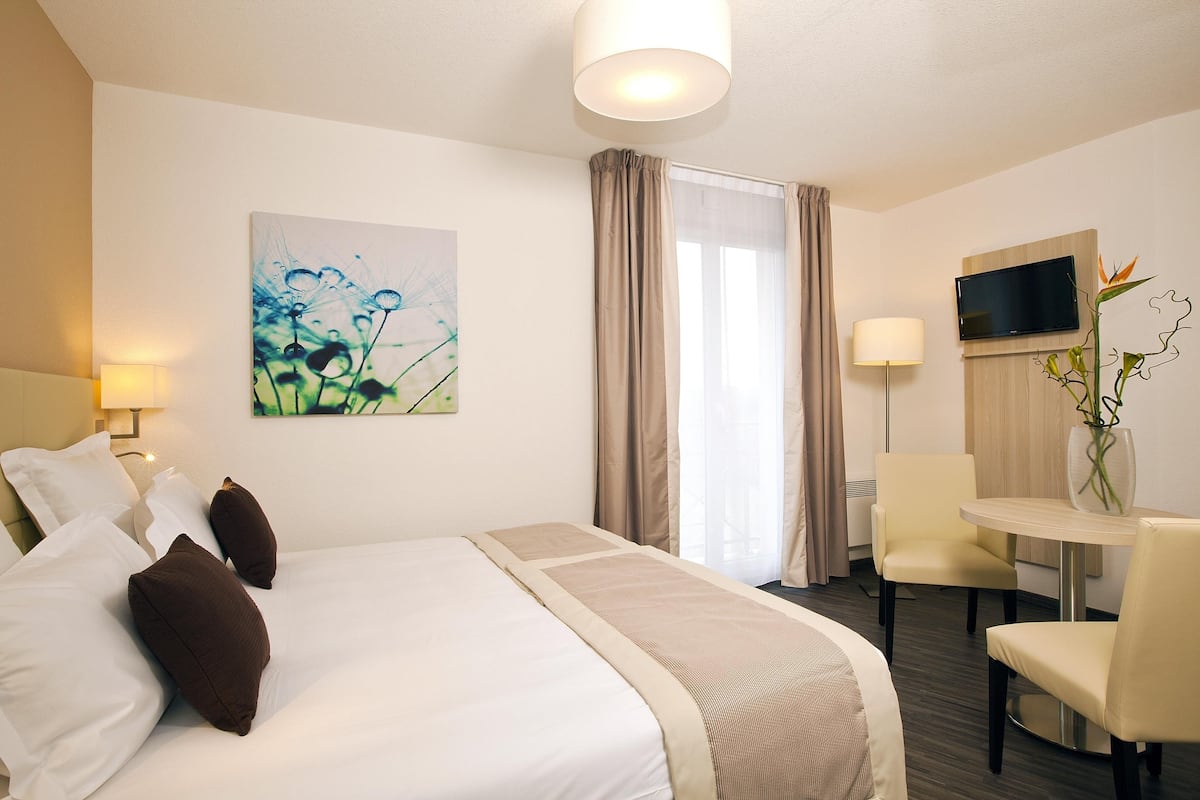Een hotelkamer met een bed, een bureau, een stoel, een televisie en een schilderij aan de muur.