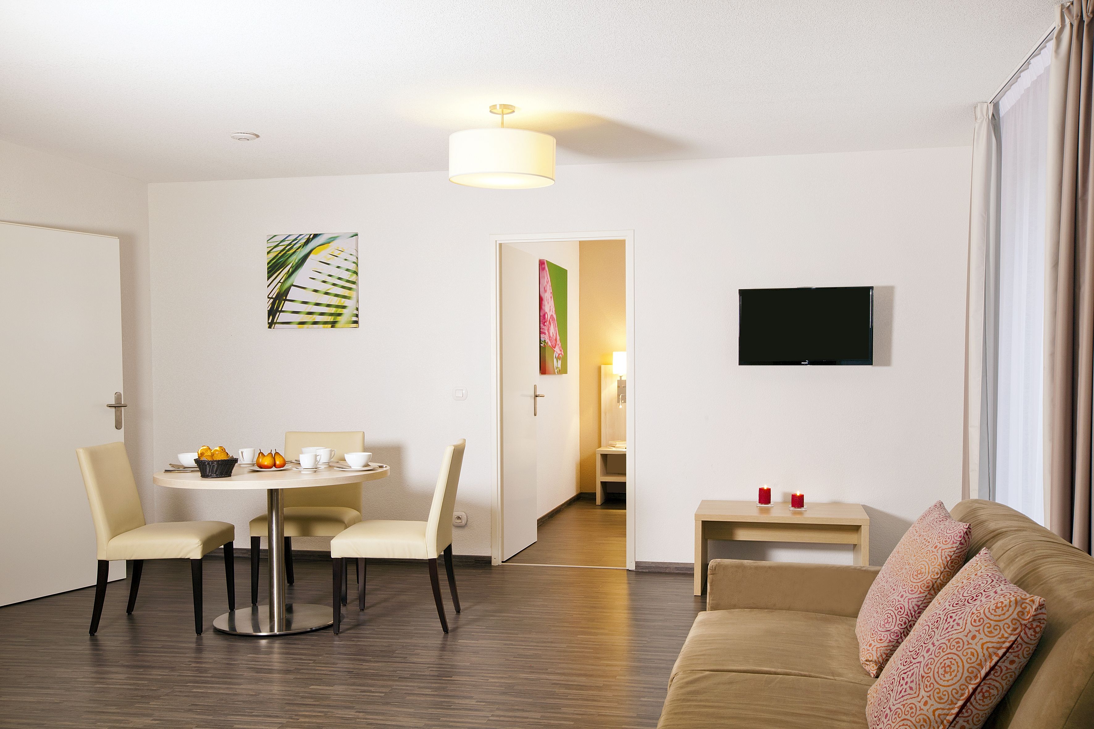 Una habitación de hotel moderna con una zona de comedor, un sofá, un televisor y una puerta que da a un baño.