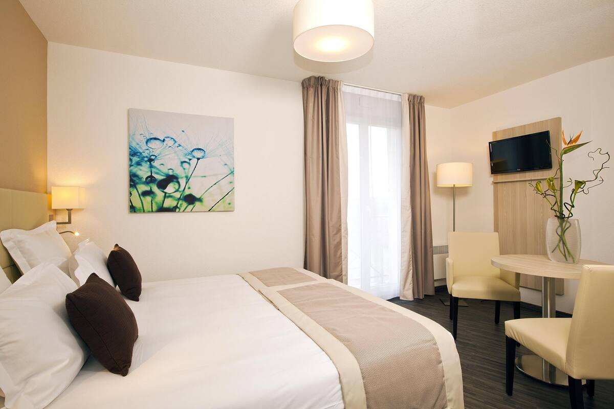 Een hotelkamer met een bed, een bureau, een stoel, een televisie en een schilderij aan de muur.