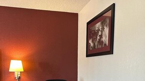 A conference room with a wooden table, a black office chair, a lamp, and a framed picture on the wall. - Red Roof Inn Fredericksburg South (Fredericksburg)