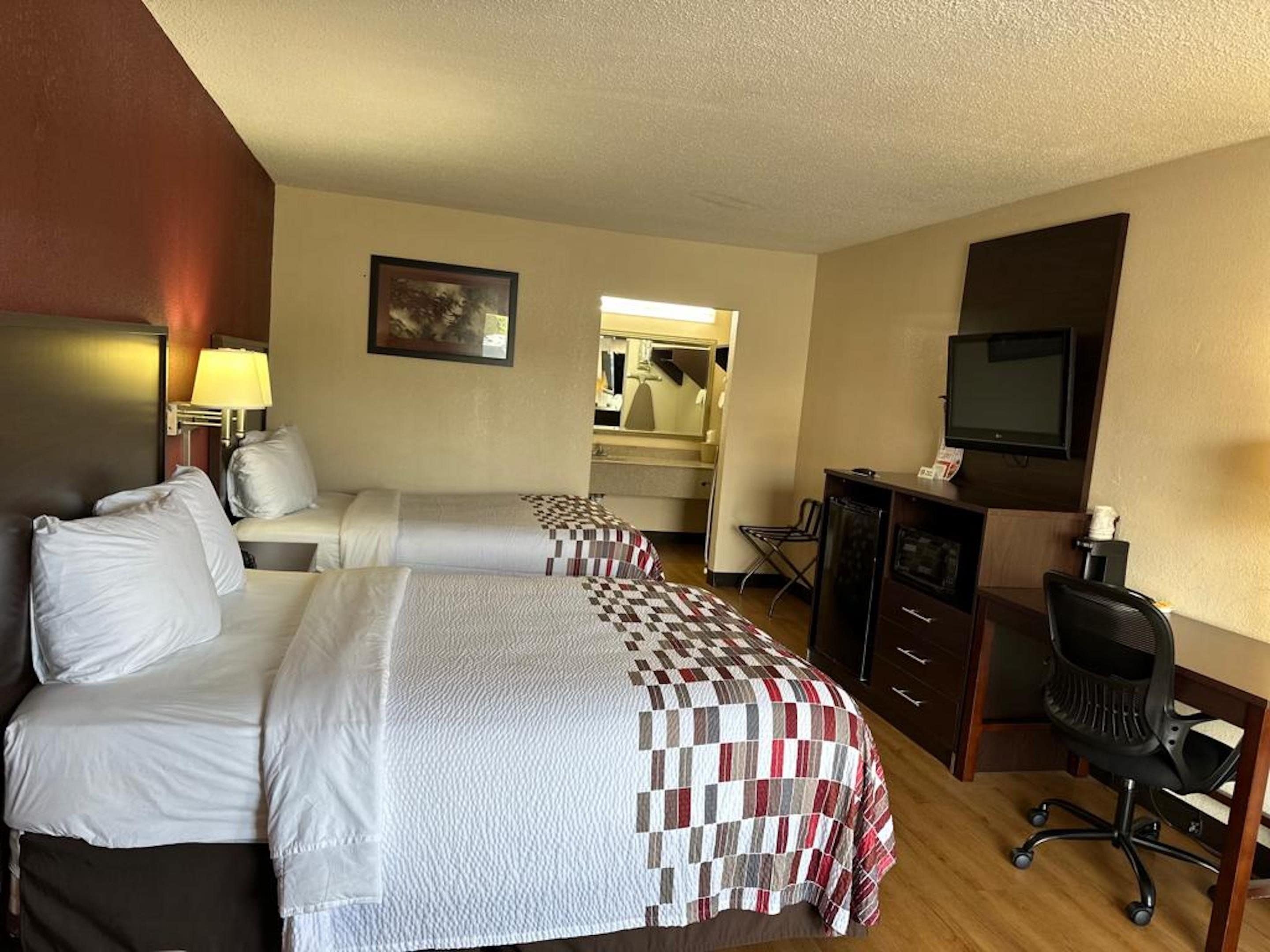A hotel room with two beds, a desk, a chair, a television, and a mirror.