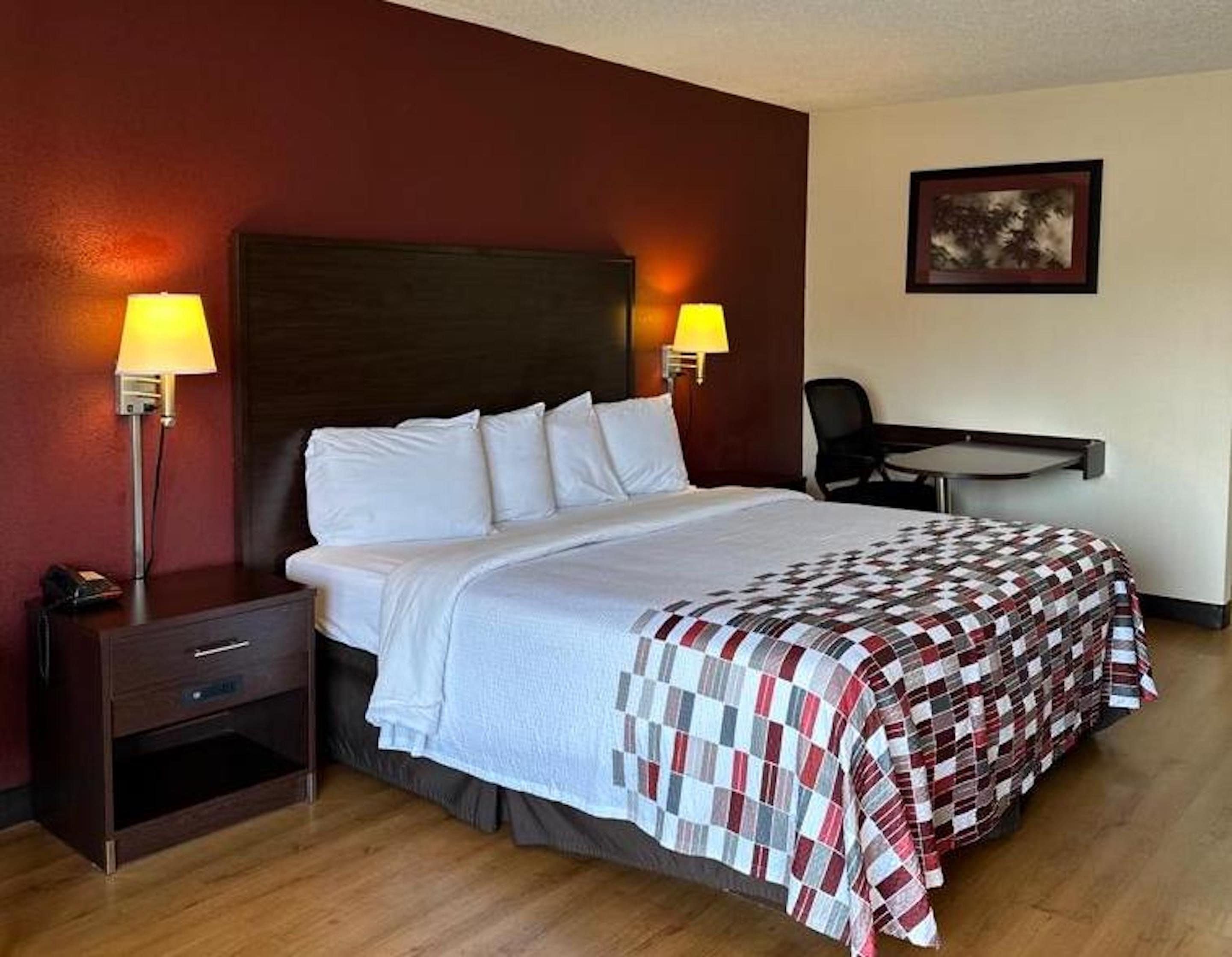 A hotel room with a bed, two bedside lamps, a desk, and a chair.