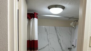 A bathroom with a bathtub, toilet, and marble walls. - Red Roof Inn Fredericksburg South (Fredericksburg)