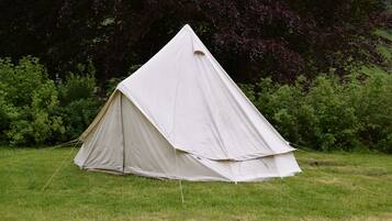 Experience the thrill of camping in a spacious pyramid-shaped tent set up amidst lush greenery.
