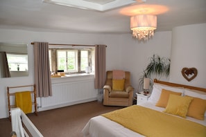 A bedroom with a bed, a chair, a bedside table, a lamp, a window with curtains, a radiator, and a chandelier. - Sweetbriar Cottage B&B and Camping (Skipton)