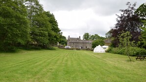 A grassy field with a stone building, a white tent, and a picnic table. - Sweetbriar Cottage B&B and Camping (Skipton)