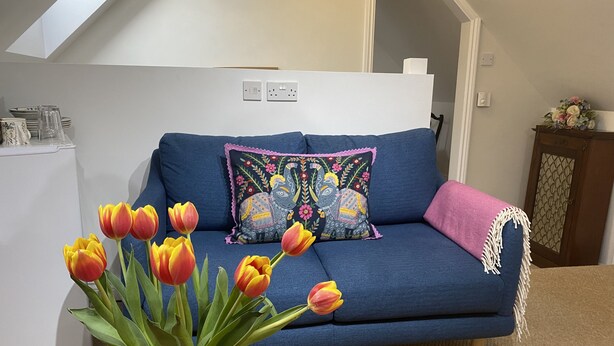 A blue sofa with a decorative pillow, a vase of tulips, and a wooden table.