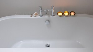 A white bathtub with two faucets and two lit candles on the side.