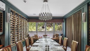 Un comedor con una mesa larga preparada para una comida, rodeada de sillas, y una estantería para vinos a la izquierda.