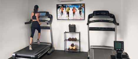A gym with treadmills, a wall-mounted TV, and a rack with towels.