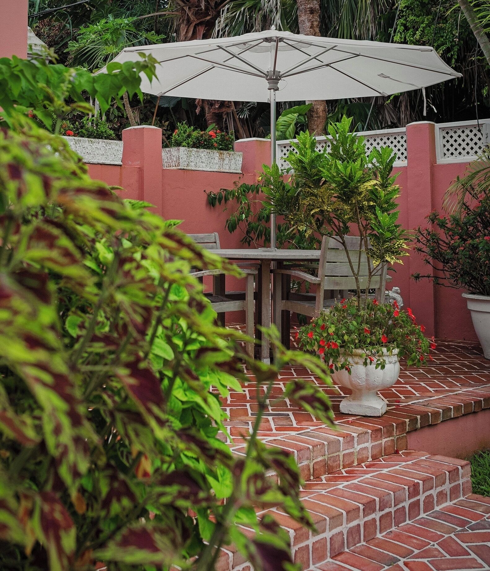 Un patio con una mesa, sillas, un paraguas blanco y plantas en macetas.