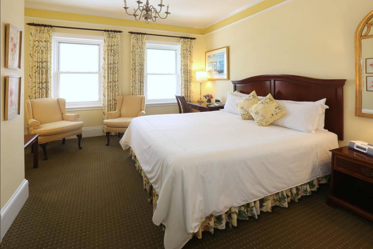 A hotel room with a large bed, two armchairs, a desk, and a chandelier.