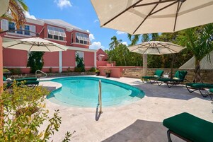 Una piscina al aire libre, sombrillas, sillones reclinables de piscina