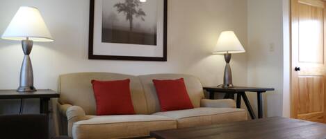 A living room with a sofa, two red pillows, a coffee table, and two lamps.