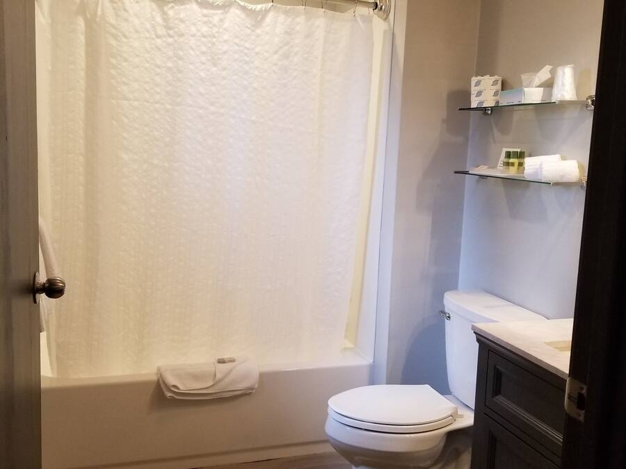 Un baño con bañera, inodoro y estante con artículos de aseo.