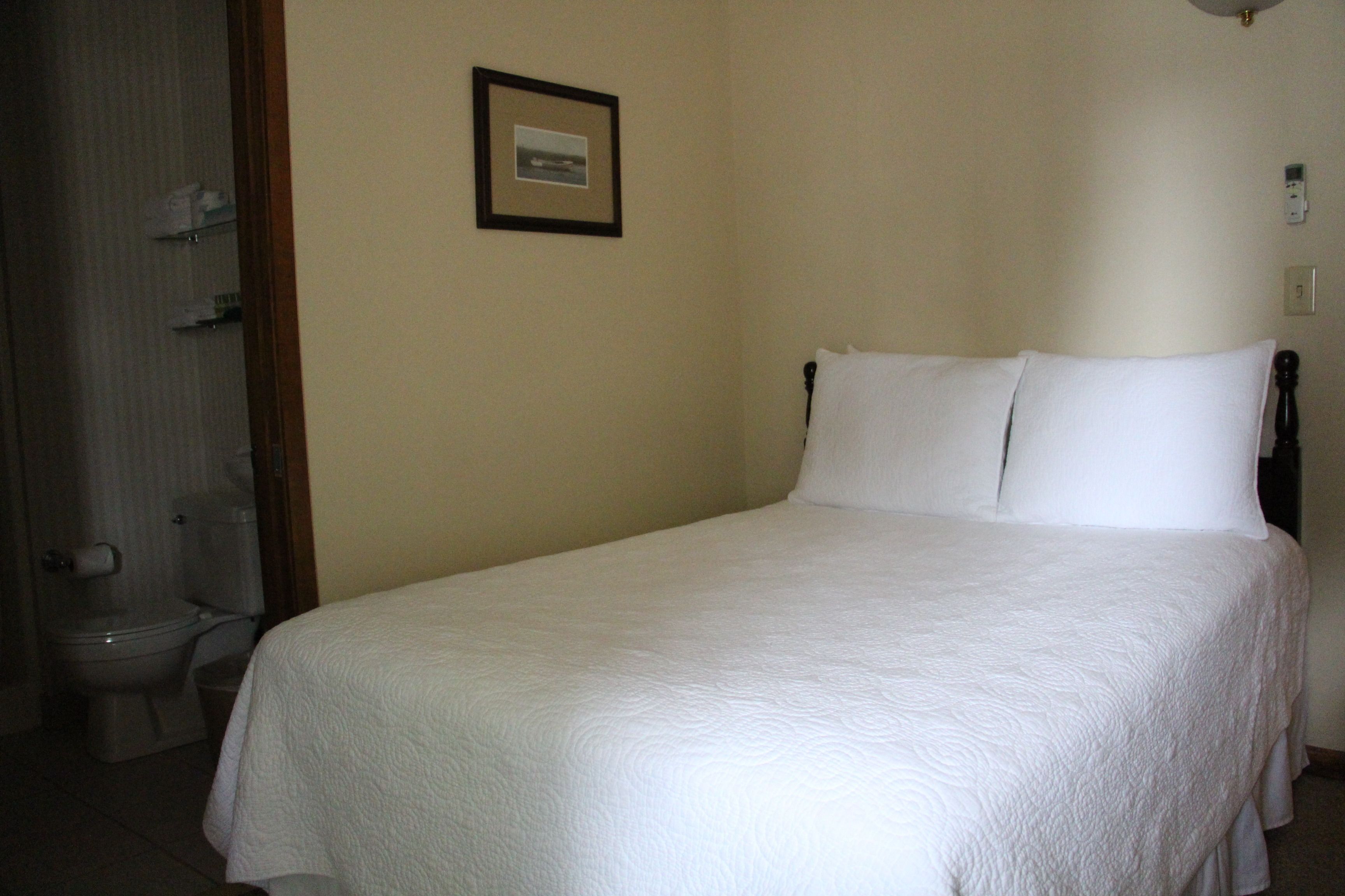 A neatly made bed with white bedding in a room with beige walls.